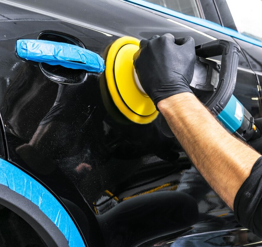 Car polish wax worker hands applying protective tape before polishing. Buffing and polishing car. Car detailing. Man holds a polisher in the hand and polishes the car