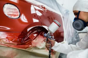 Man with protective clothes and mask painting car using spray compressor.