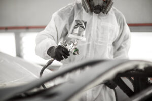 Car painter spraying a car part with a pressurized spray gun in a painting chamber.