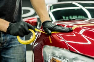 Car service worker applying protective tape on the car details before polishing