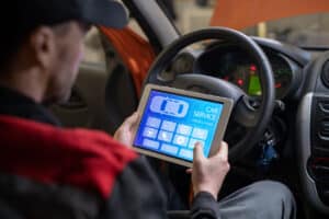 Close up of car mechanic using digital tablet with service and maintenance app on screen while inspecting vehicle in auto repair shop