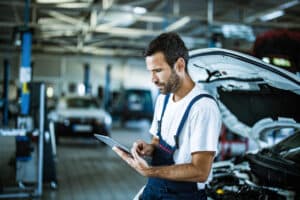 Young manual worker using touchpad while working in auto repair shop.