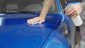 Close up of master with tattooing hands preparing the hood of deep blue sport car for polish in workshop, slow motion