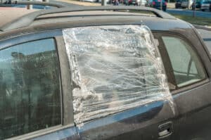 Broken and damaged shattered glass of the car side window protected with nylon and duct taped to protect interior from rain and water