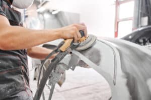 Mechanic using a grinding tool to sand off car paint