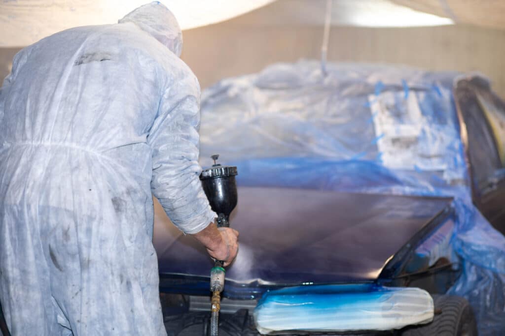 Man in overalls sprays paint on vehicle