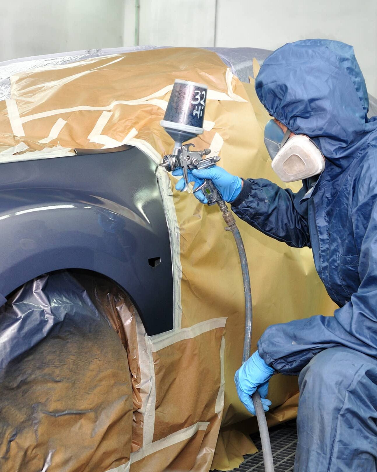 Worker painting car in a paint booth. Man painting a silver car.