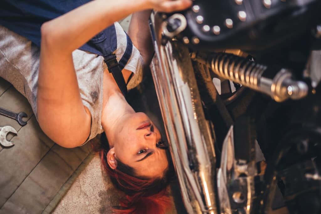 Female mechanic fixing the bottom of a car