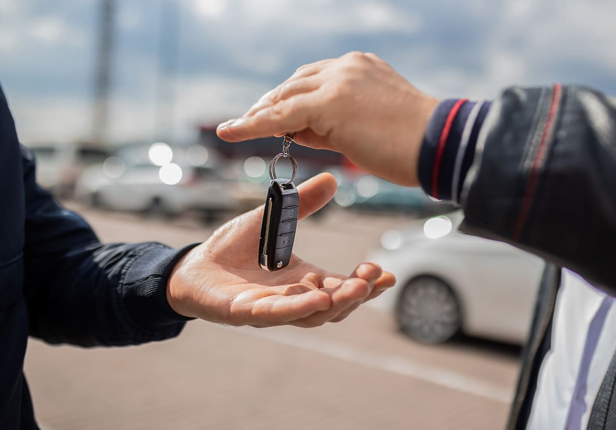 Two male hands passing over keys to new car.