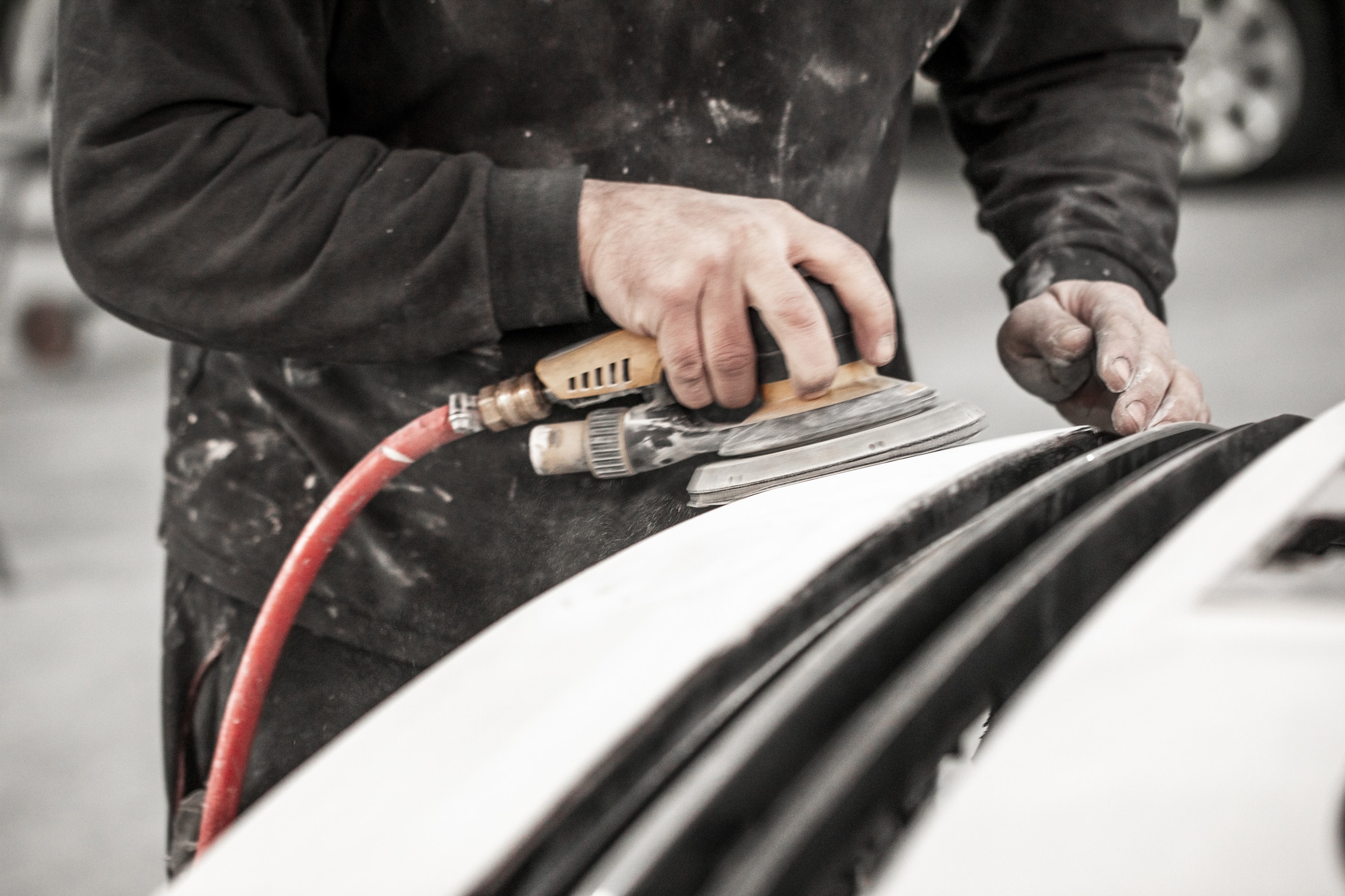 Body repair technician removing excess filling from an accident-damaged car bumper using a pneumatic sander.
