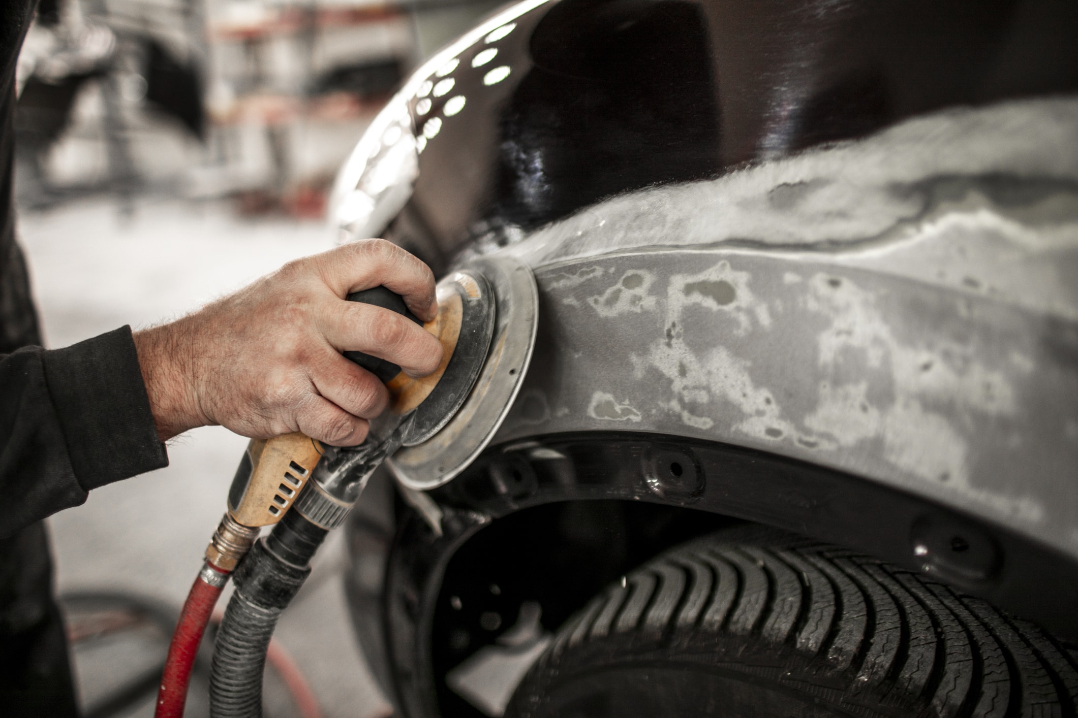Using an electric orbital sander to sand out a filler on a damaged quarter panel.