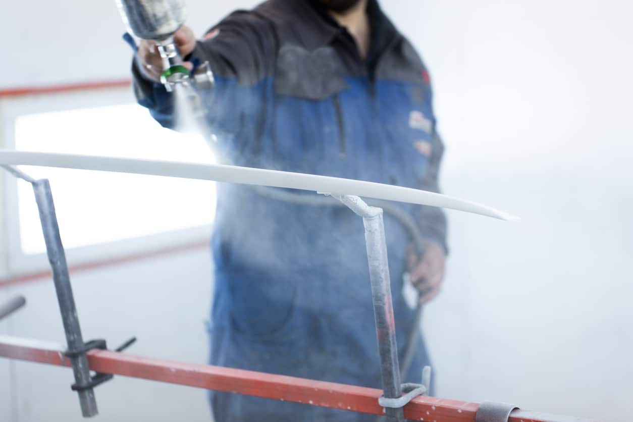 A painter in protective overalls and a respirator to paint the car body in the paint chamber.
