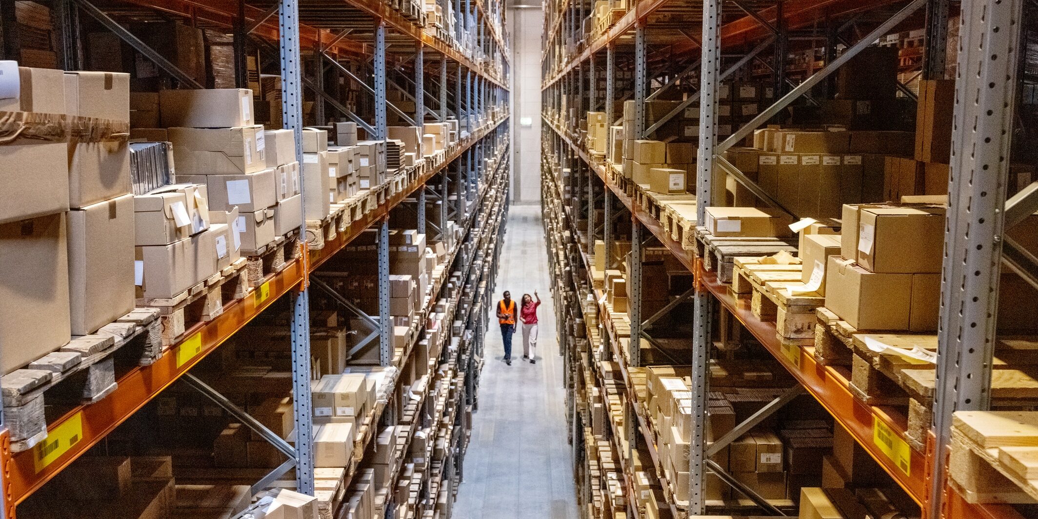 High angle view of a warehouse manager walking with foremen checking stock on racks. Businesswoman discussing stock with a male worker while walking by racks in warehouse.