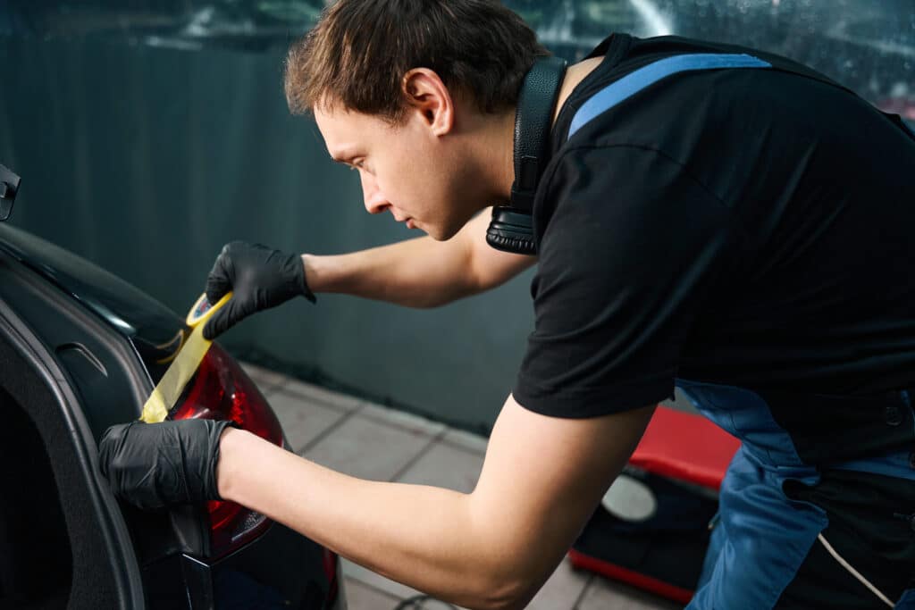 Serious auto detailer in nitrile gloves applying masking tape to automotive taillight