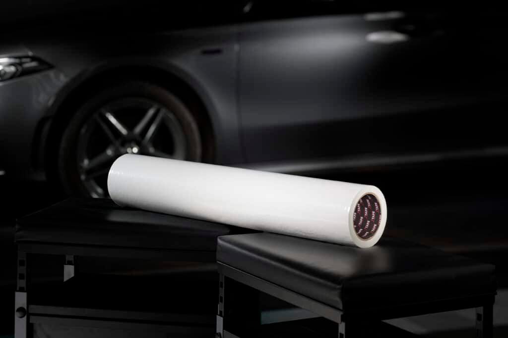 A large white roll of film is prominently displayed against a dark, sleek background with a car.