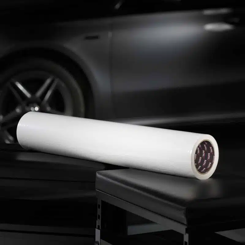 A large white roll of film is prominently displayed against a dark, sleek background with a car.