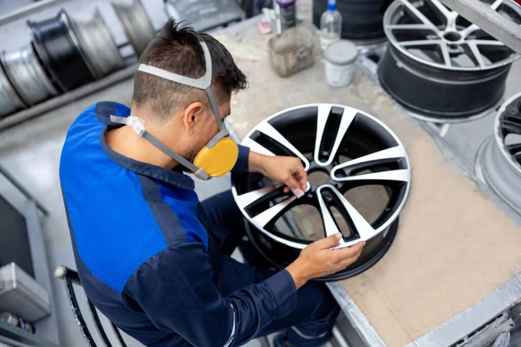 Latin American worker sanding an alloy wheel at a car part factory and using a face mask
