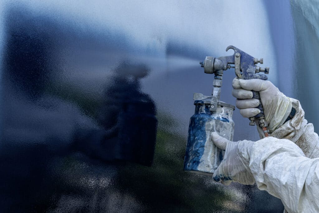 A worker in a body protective suit paints the hull of a sailing yacht with spray.