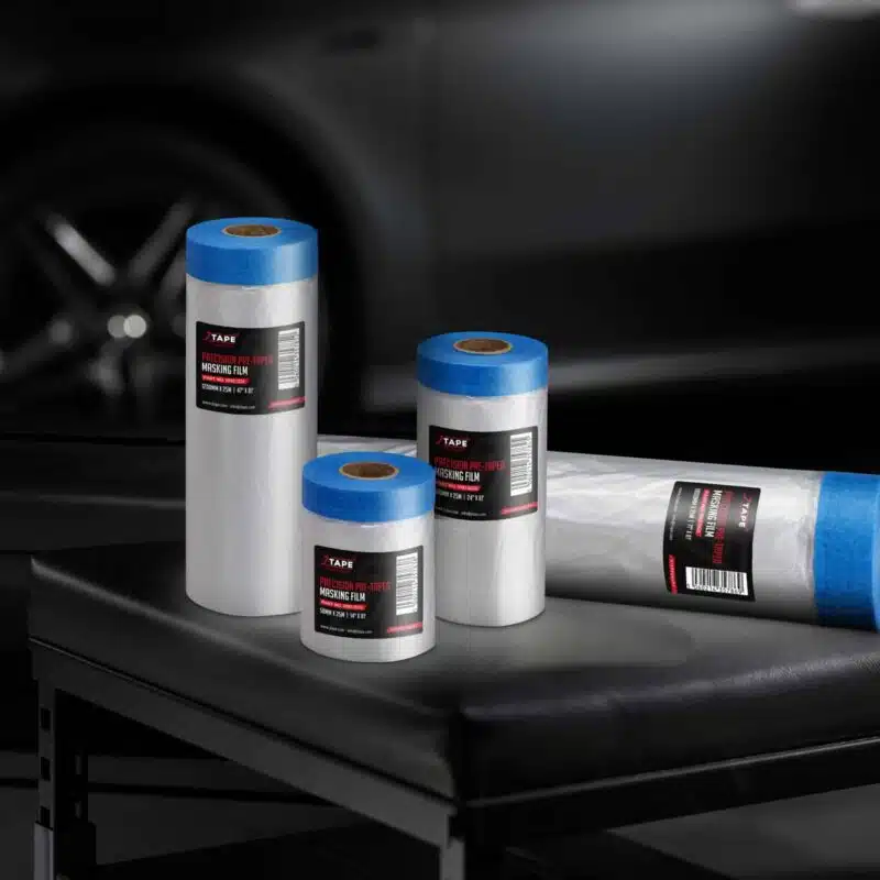 4 rolls of JTAPE's Precision Pre-Taped Masking Film on a black leather bench, set against a blurred dark car background